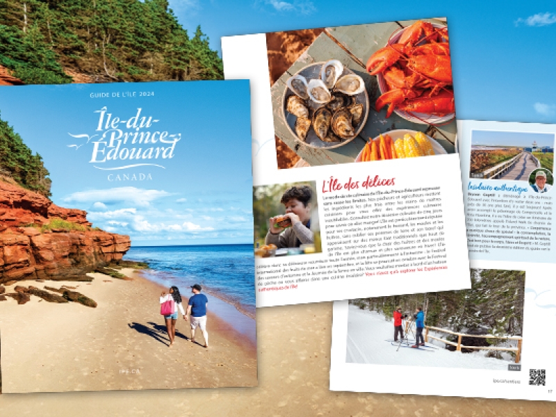Three pages of French PEI visitors guide in foreground with image of red cliffs in background