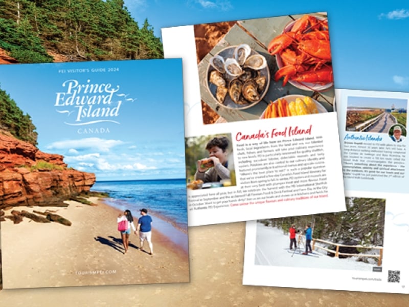 Three pages of PEI visitors guide in foreground with image of red cliffs in background
