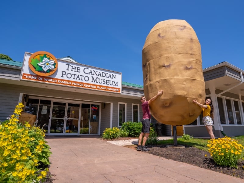 Two people stand with arms around big potato in front of the Canadian Potato Museum 