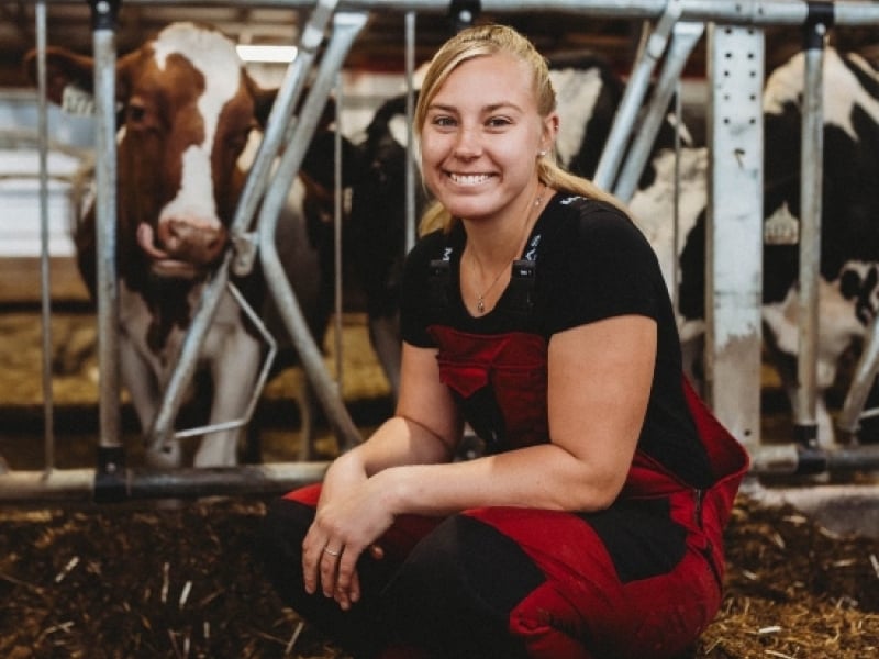 Suzanne Brouwer kneels in front of dairy cows in stall