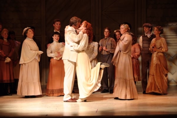 The characters of Anne & Gilbert kiss on stage with the company in the background
