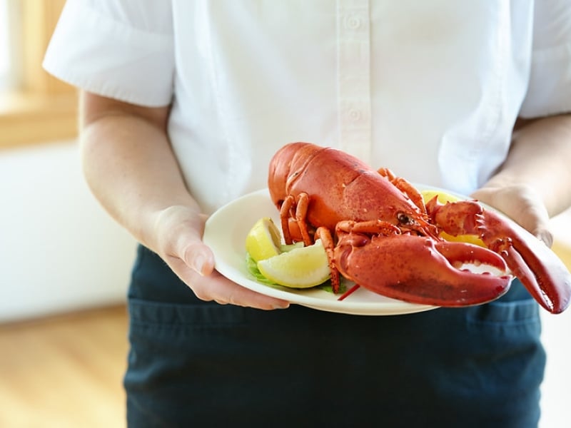 server holds plate of cooked lobster with lemon wedges