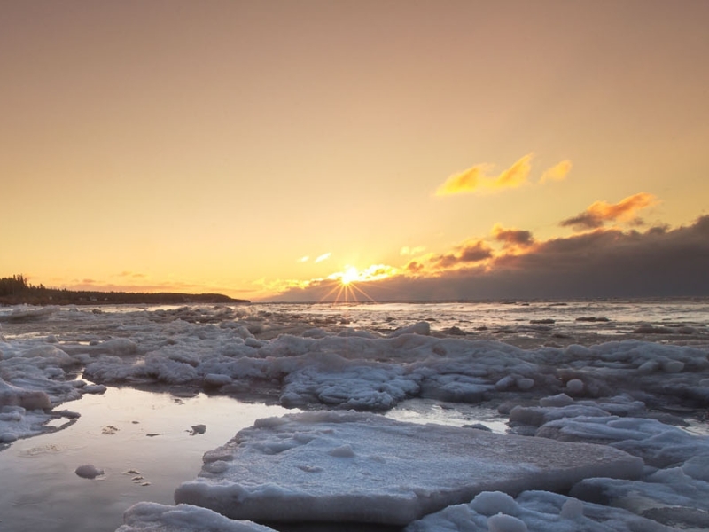 Sun sets over ice-covered waters near red cliff