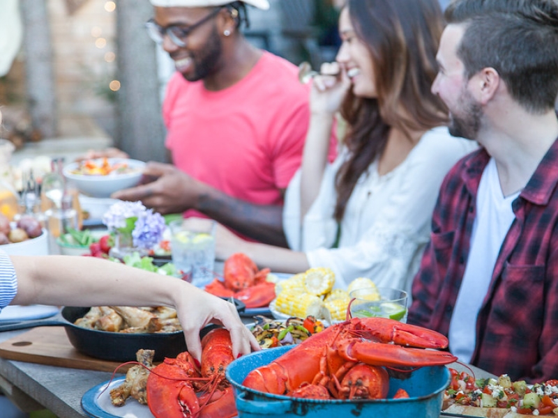 Group dining on lobster, potatoes, corn and other fall flavours at picnic table outdoors 