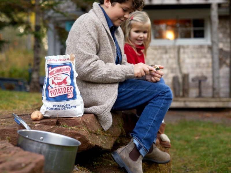 Image of young boy and child sitting outside a cabin peeling potatoes