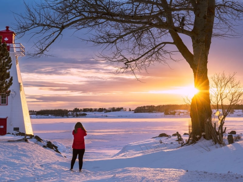 Female in red jacket next to Victoria Park Light looking over Charlottetown at sunset in winter