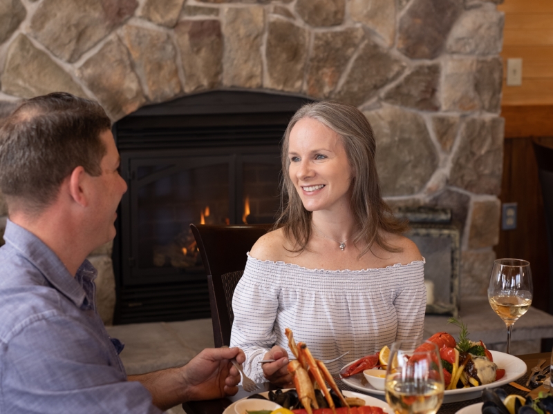 Couple sit at table in front of fire place enjoying seafood dinner