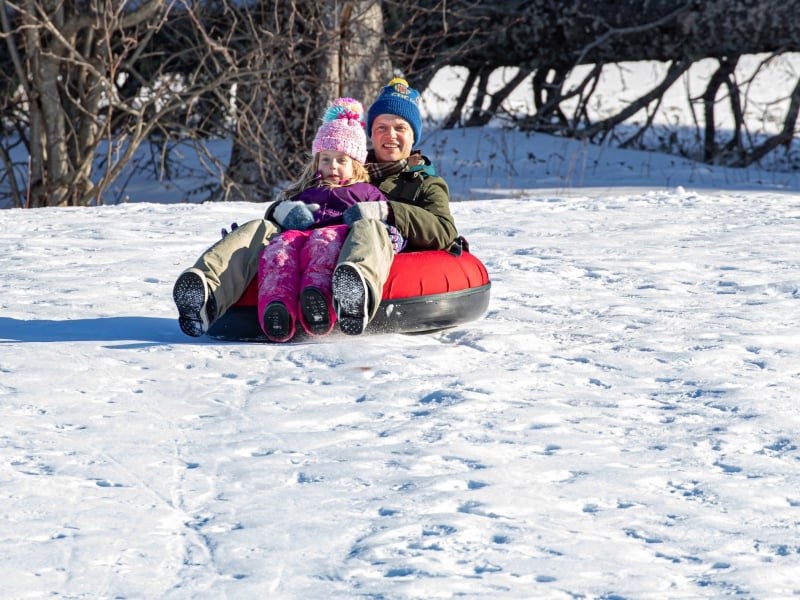 Parent and child in tube sliding down hill at Brookvale Nordic Park