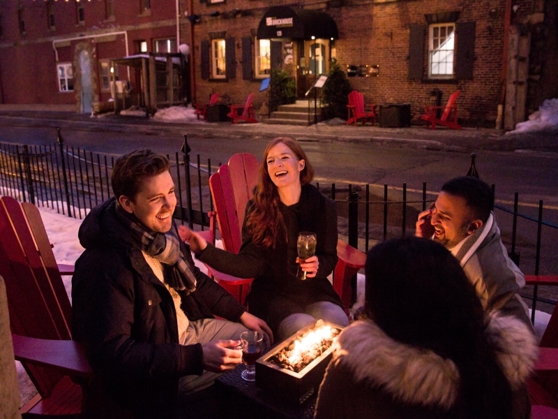 Group of four sit on outdoor deck with firepit on Sydney Street on a winter night