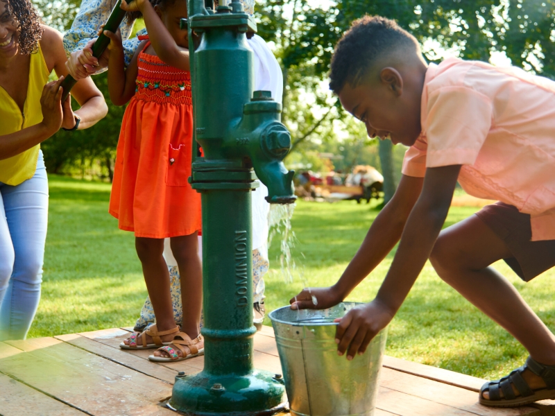 Young boy and adult pump water from hand pump at Orwell Corner