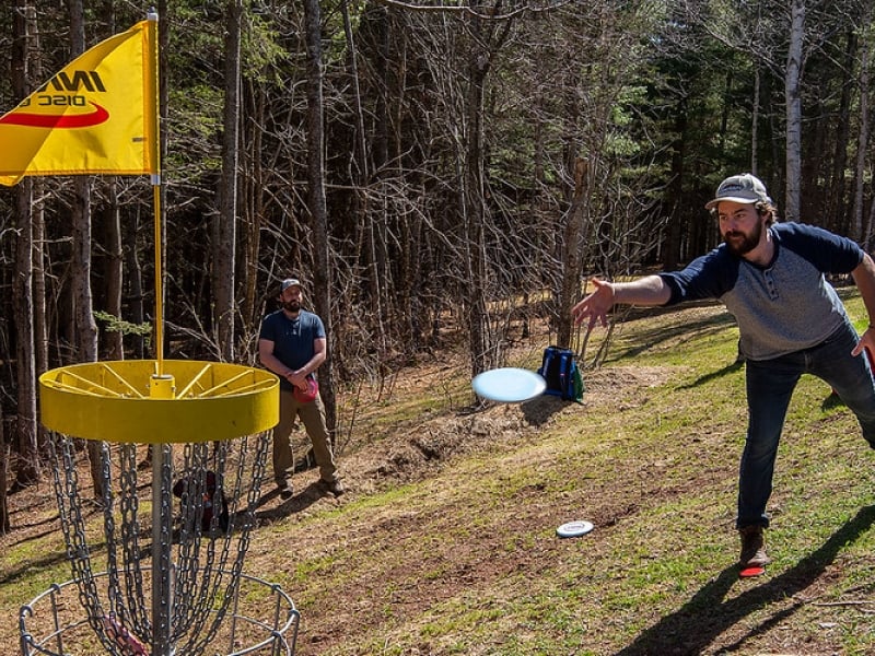 Two disc golf players shoot for basket at Hillcrest Disc Golf Course