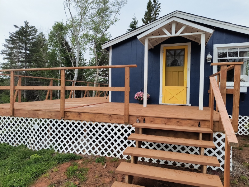 Blue one story cottage with welcoming bright yellow door and large front deck
