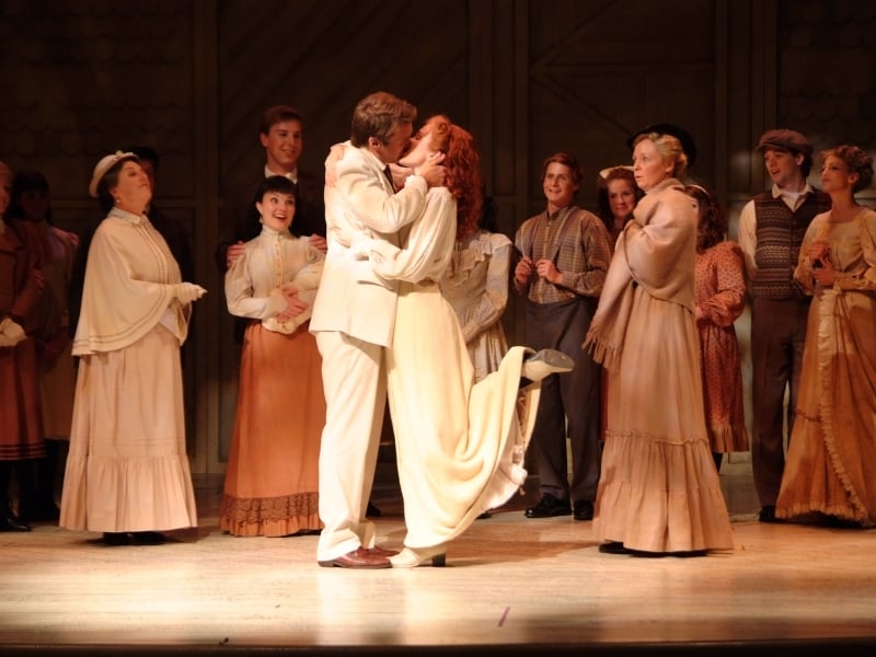 The characters of Anne & Gilbert kiss on stage with the company in the background
