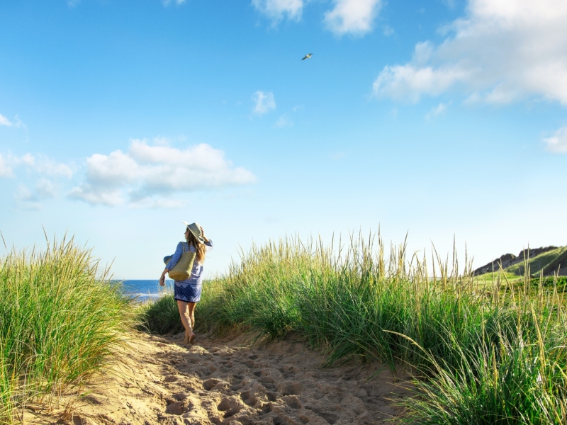 Women walks to beach via trail through dune