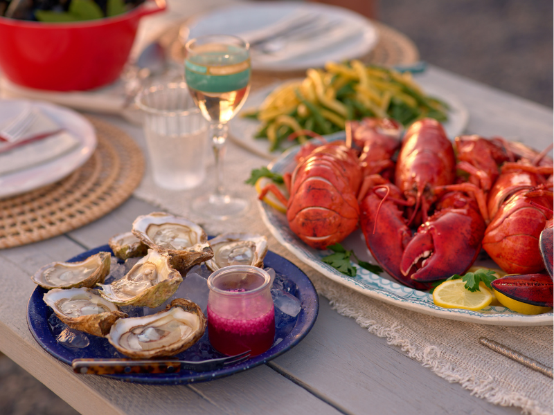 Picnic table is set with platter of PEI Lobster, PEI oysters, summer vegetables, etc