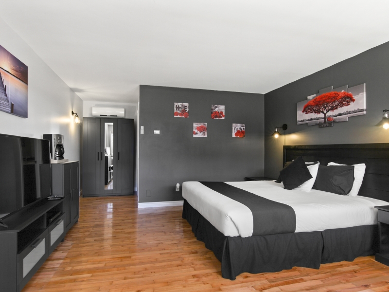 Large bedroom wit hardwood floors, grey and white accent walls highlighted by red accent decor