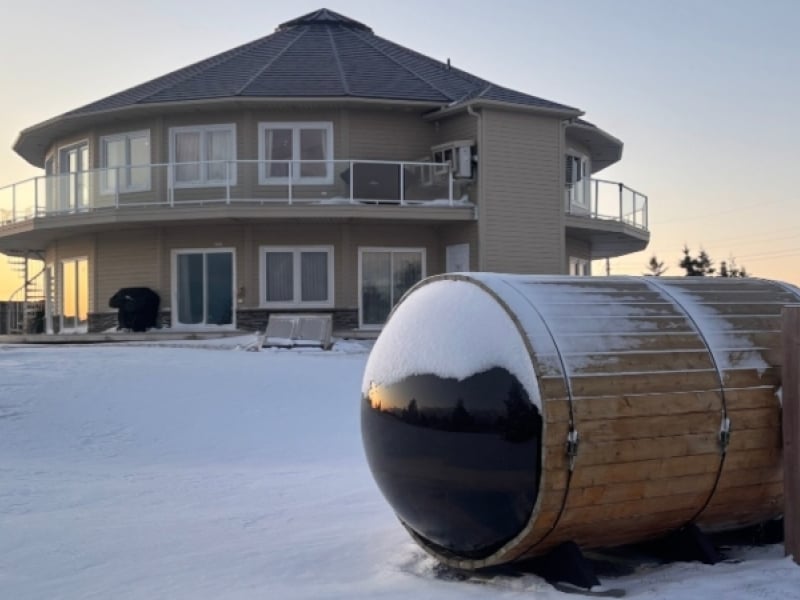 Canada's Rotating House at sunset in winter with barrell sauna in foreground
