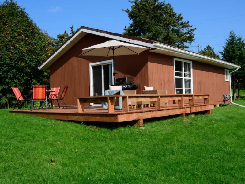 Brown cottage with wrap around deck and outdoor chairs and bbq