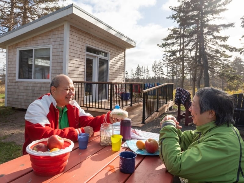 Couple sits at picnic table at a BUNKIE site in PEI National Park
