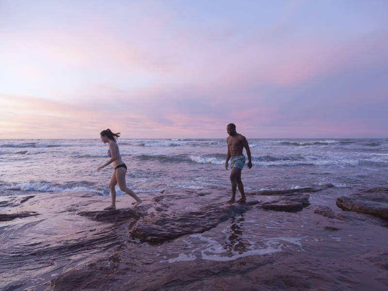 Couple walk on rocks at Cavendish Beach at sunset