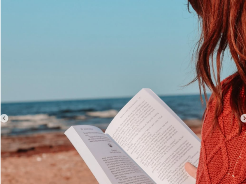 Red haired person sits on PEI beach reading a book