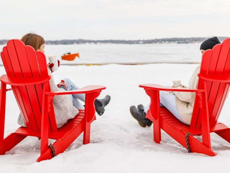 Two people sit in red adirondak chairs overlooking Charlottetown Harbour in winter