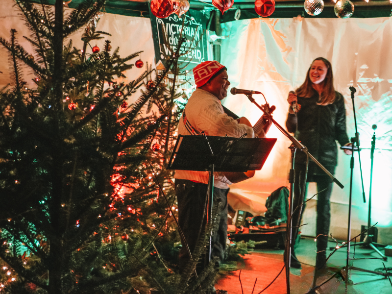 Two musicians sing next to evergreen tree in market booth