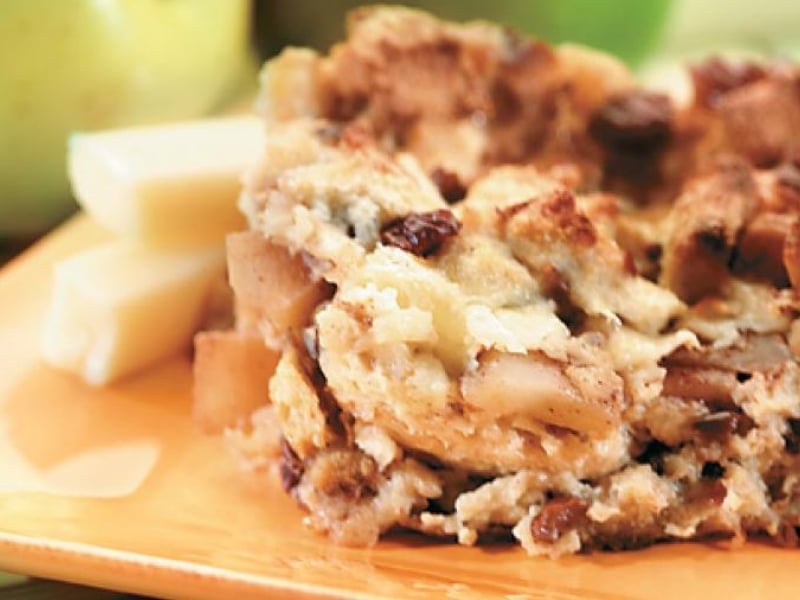 Piece of Cinnamon Apple Strata and pieces of white cheddar sitting on a cutting board