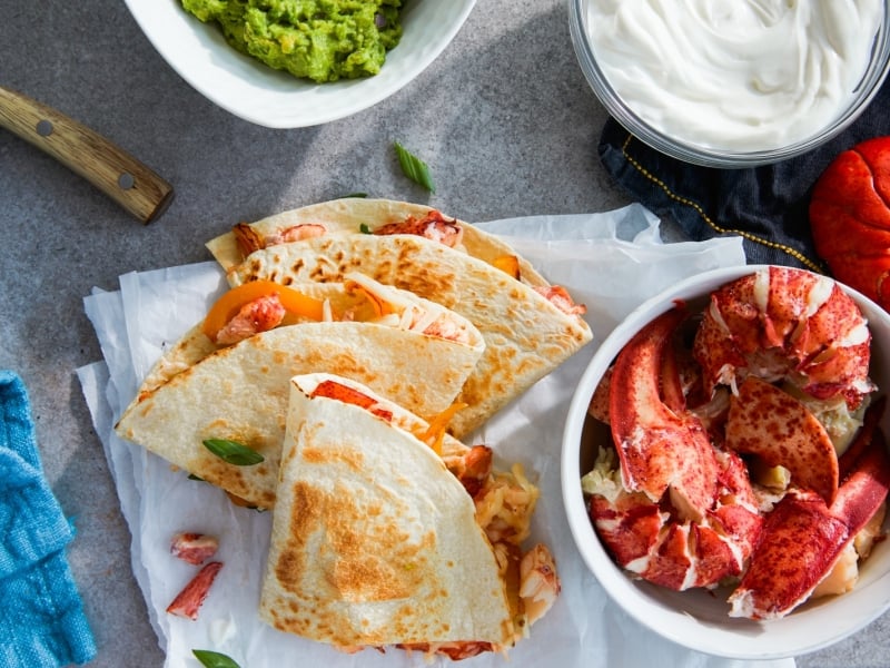 Styled image of lobster quesadillas with a bowl of fresh lobster meat, avacado and sour cream