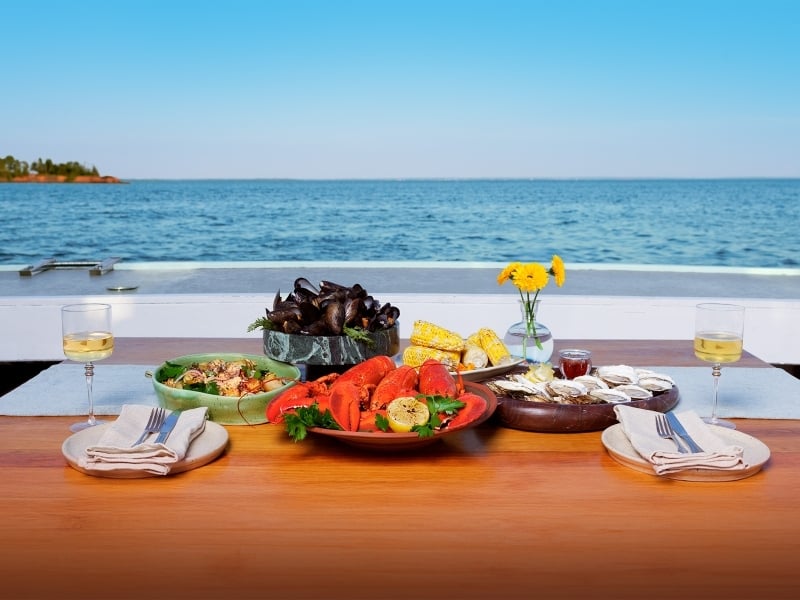 A feast of PEI lobster, mussels, oysters potatoes, corn and salad served on a fishing boat with coastline in background