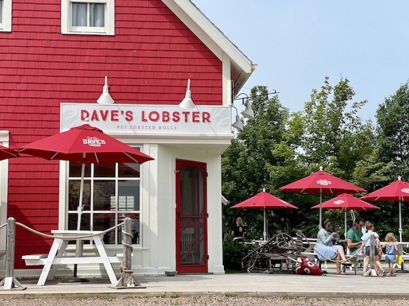 outside view of the corner of the red building which houses Dave's lobster. picnic tables and umbrellas around outside of building