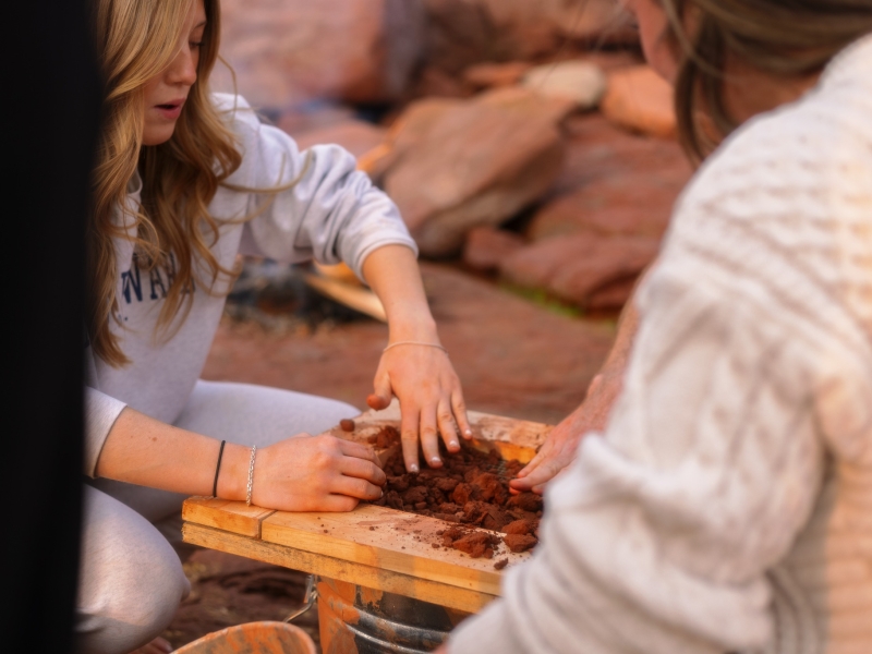 Two people filtering red Island clay through screen on PEI beach