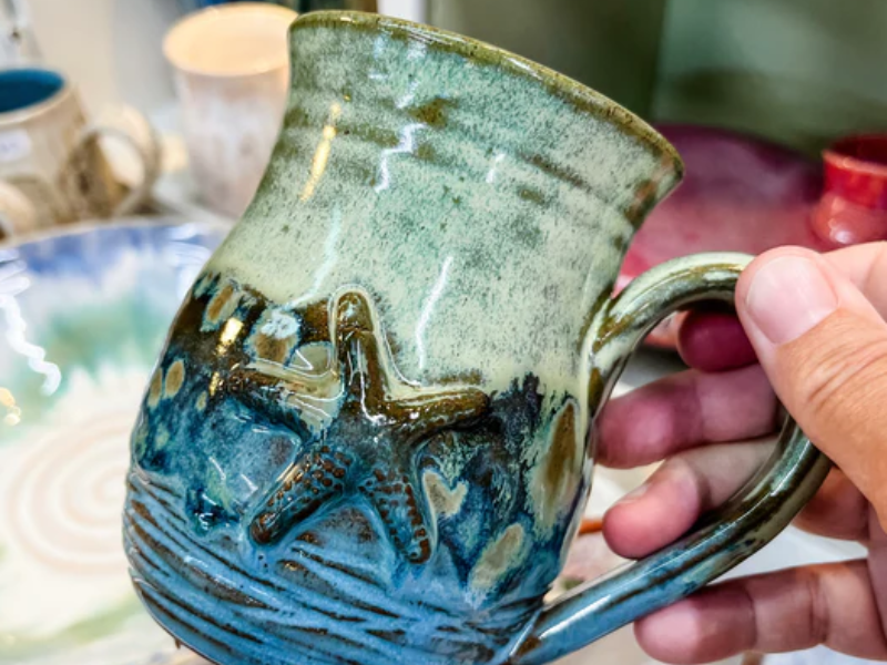 A person holds a blue and green pottery mug with star fish