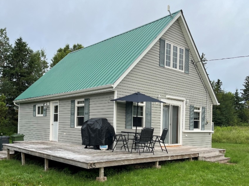 Outdoor image of Fogwell Cottage, light green siding with brighter green steel roof, wrap around deck