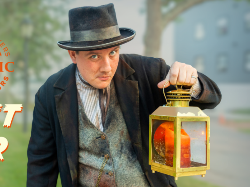 Heritage actor hold lantern with graphic text "Historic Heritage Players Walking Ghost Tour"