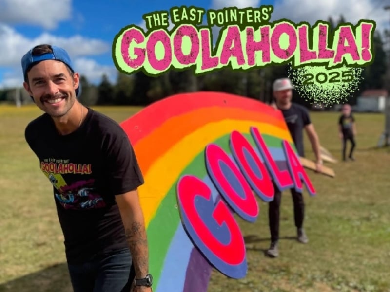 Image of two members of the East Pointers carrying the Goolaholla sign on the concert site. Graphic of "The East Pointers' Goolaholla 2025" overlaid on top of image.