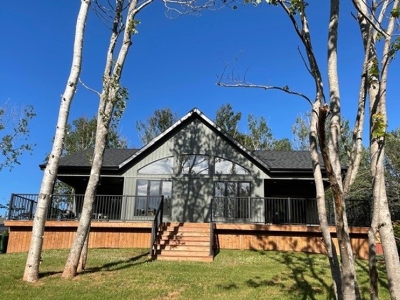 Large grey siding home with front wrap around deck. Widows overlooking the yard and Birch trees.
