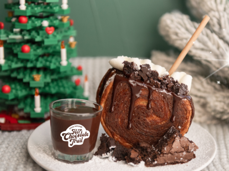 A plate with a chocolate croissant and shot of hot chocolate with Christmas decor in background