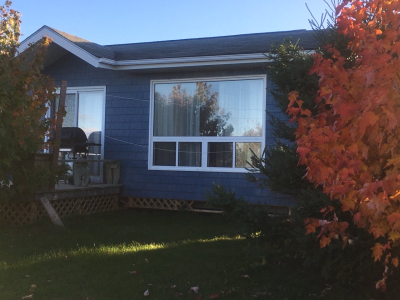 Blue bungalow with deck and trees facing the front of the property.