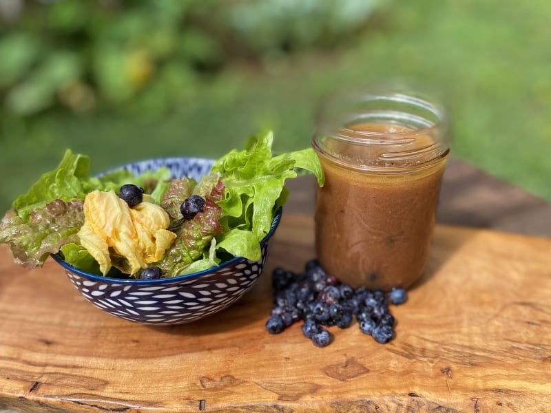 Fresh garden salad with PEI Wild Blueberry Vinaigrette in jar on side with garden in background