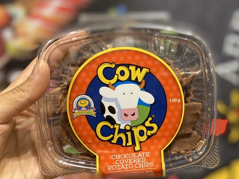Package of COWS chocolate covered potato chips held in from of display of candy