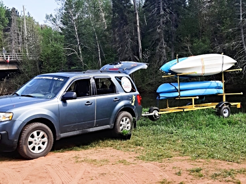View of truck and trailer with multiple kayaks parked next to a river