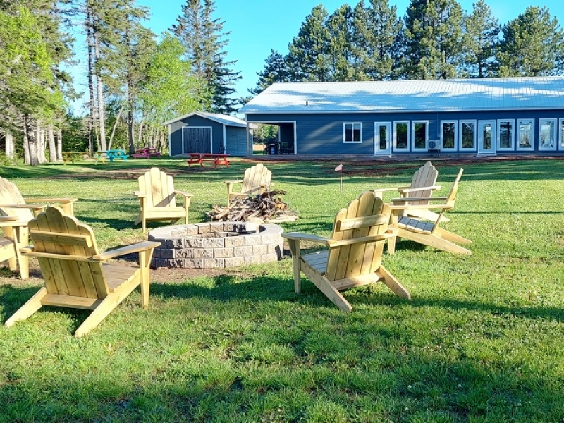 Blue one storey lodge with large grounds, campfire pit circled by Adirondack chairs