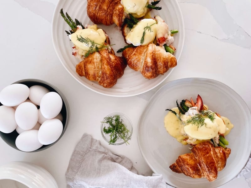 Overhead shot of bowl of fresh eggs and two plates of  Lobster & Asparagus Eggs Benedict with Lemon Dill Hollandaise 