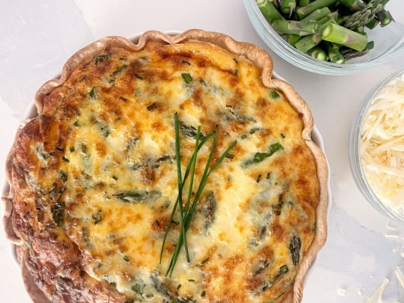Overhead view of lobster and cheddar quiche with side dishes of white cheddar and asparagus
