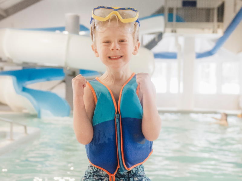 Close up of small boy on indoor pool deck with waterslide in background