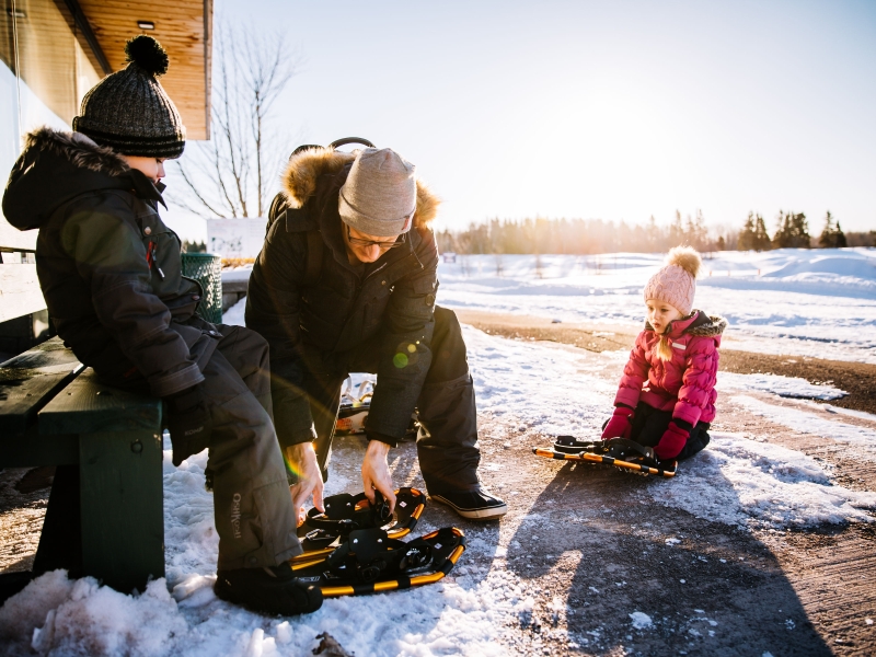 Male helps children put on snow shoes