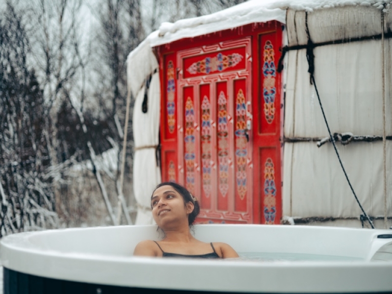 Woman in outdoor hot tub with yurt in background in winter