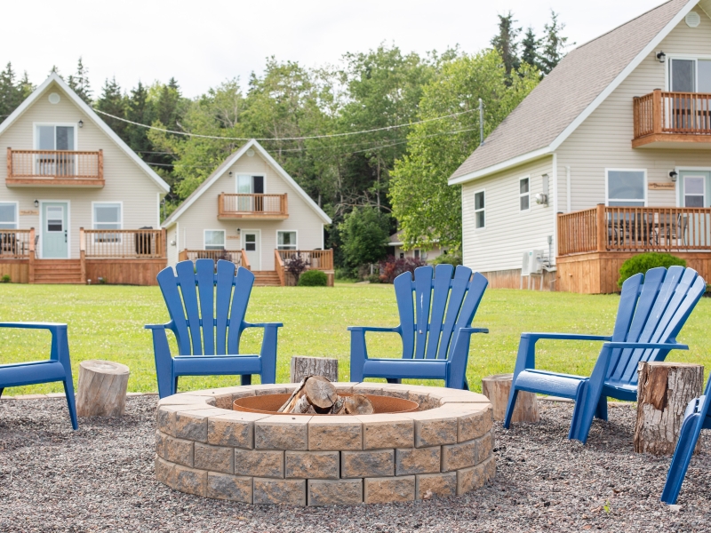 Blue adirondack chairs situated around a firepit in front of Oceanview Chalets