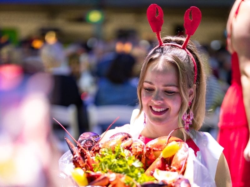 Person wearing lobster claw headband serving a platter of lobster